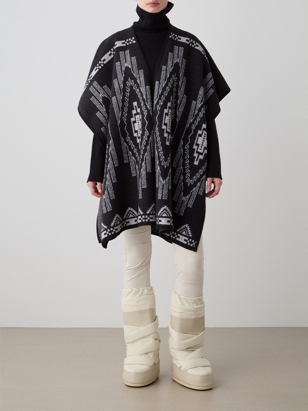 We Norwegians_FW25_Womens | Model is wearing the Pioneer poncho | Black in color with a jacquard pattern | Made with boiled merino wool | Front view