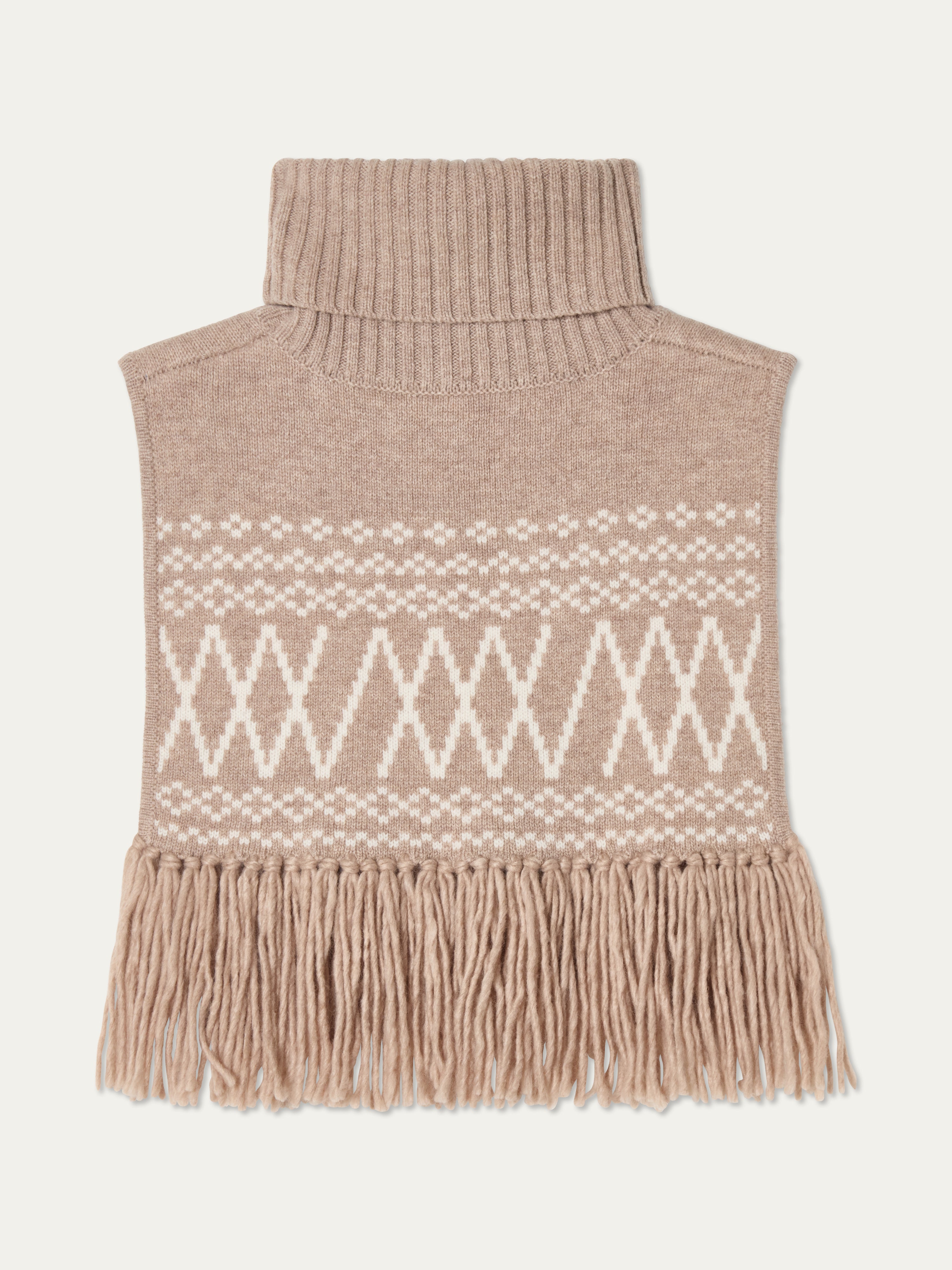 We Norwegians | FW25 | Setesdal Bib_Sand | A knitted bib with a turtle neck and fine fringes at the hem against an off-white background
