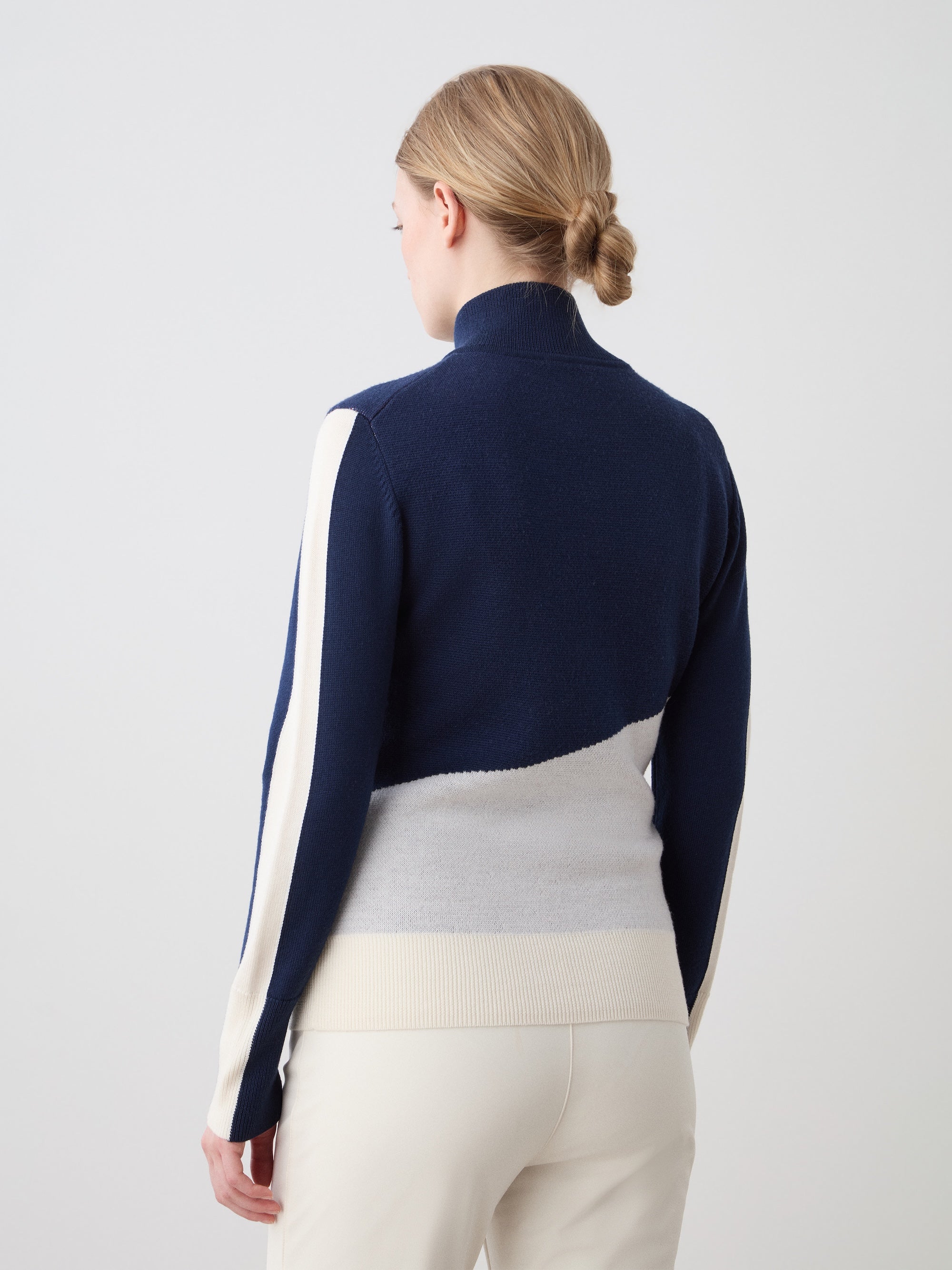 We Norwegians | FW25 | The model is wearing womens Afterski zip-up in navy blue which has the logo and 1/4th zipper in the front, against an off white background | Back view