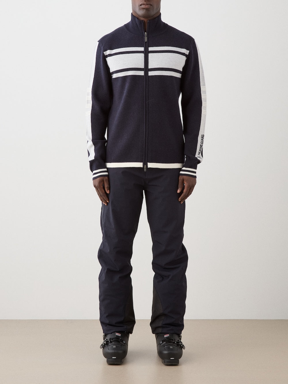 We Norwegians | FW25 | Mens Rocky Full ZipUp_Navy blue | Model wearing this fine knitted sweater with a 2-way front zipper opening, designed in a retro style with contrasting color blocks on the chest and sleeves - paired with black ski pants | Shot against an off-white background | Front