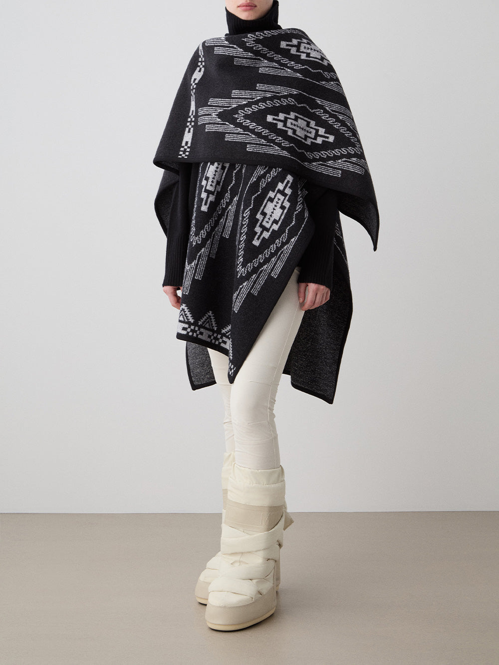 We Norwegians_FW25_Womens | Model is wearing the Pioneer poncho | Black in color with a jacquard pattern | Made with boiled merino wool | Photograph showing the fall and drape features of the garment