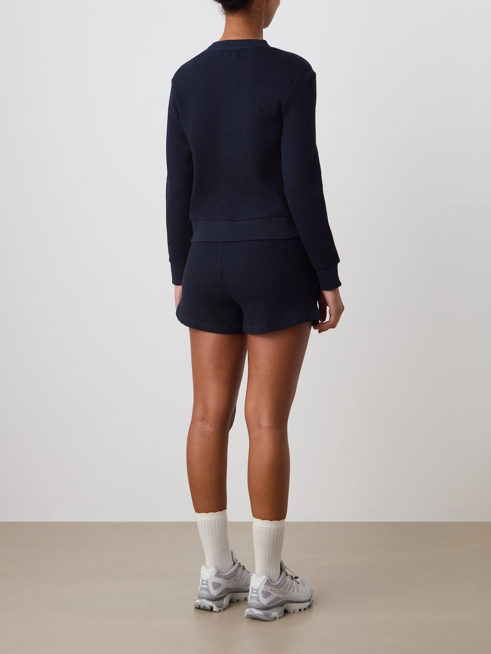 Person wearing a navy blue waffle creweck with shorts and sneakers on a plain background
