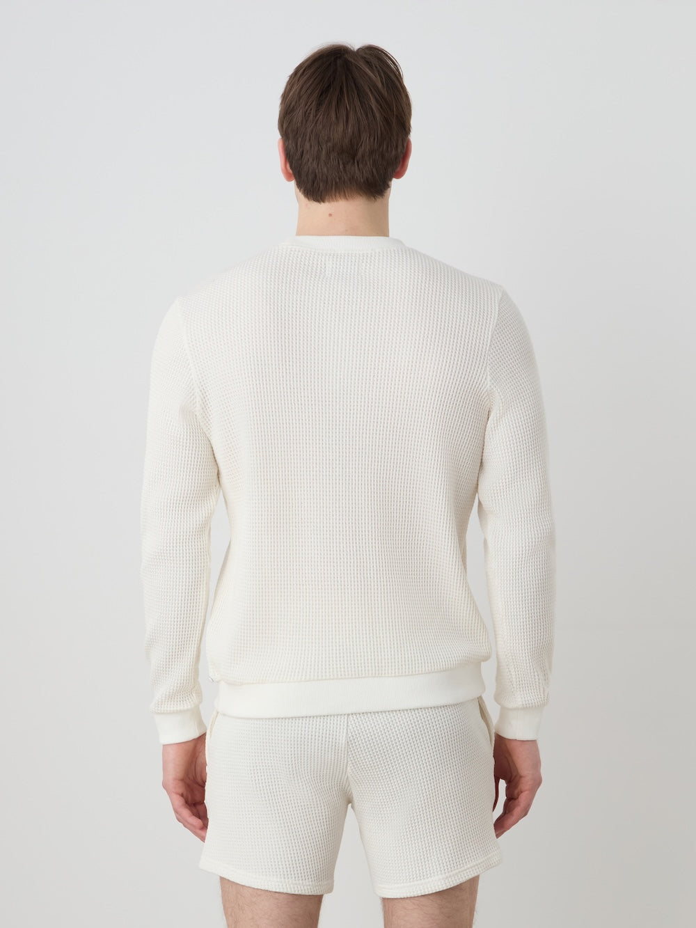 Person wearing an off white crewneck and shorts on a light background