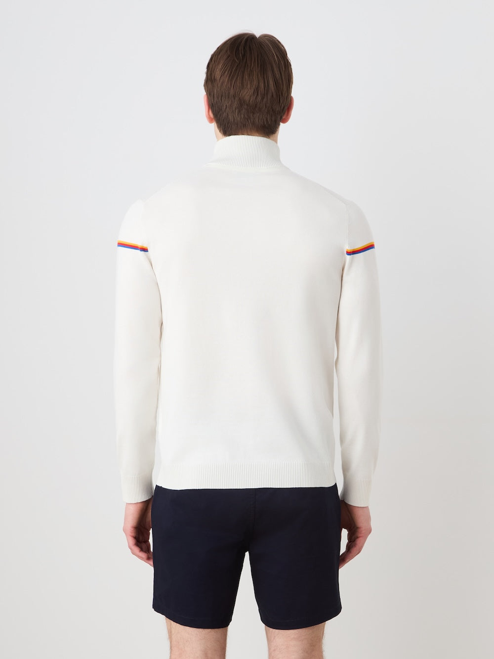 Person wearing an off white "Grand Slam" sweater with color accents and navy shorts on a light background
